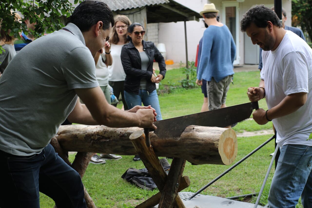 Two of us sawing a log with a two-man saw on a farm in Lithuania while the others watch