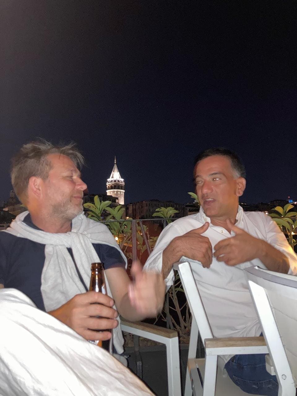 Two of us talking on a rooftop at night, with Galata Tower lit up behind