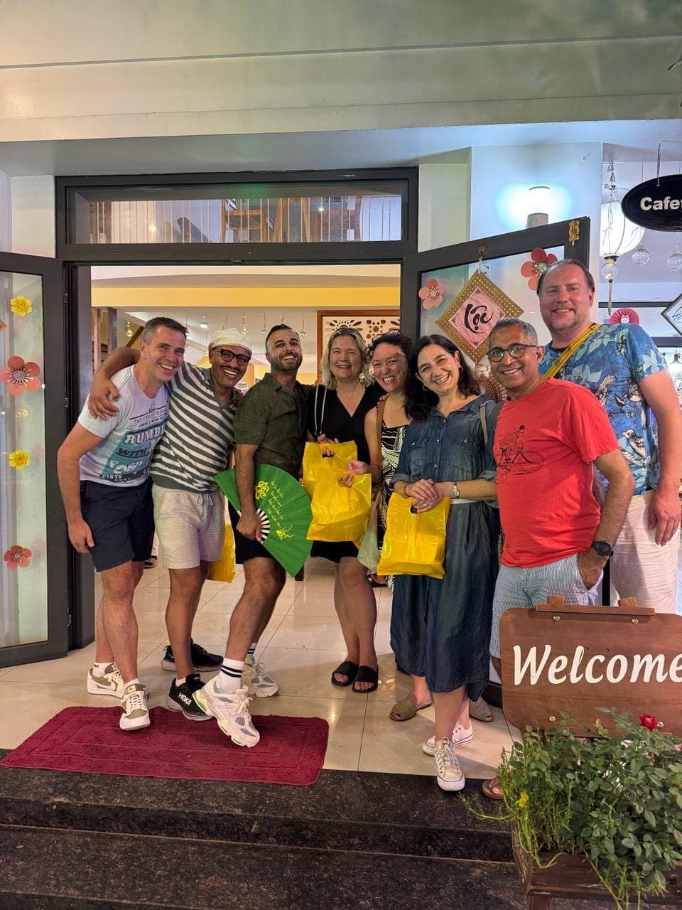 Eight of us at a shop door, with yellow shopping bags and a green paper fan